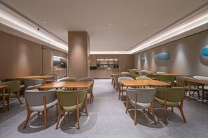 Un espace repas moderne avec des tables et des chaises en bois, une cuisine en arrière-plan et un design minimaliste.