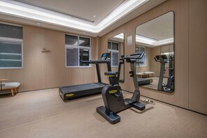 Un gimnasio moderno con cinta de correr, elíptica y bicicleta estática, espejos amplios y suelo de madera.