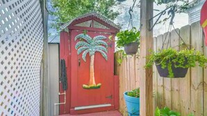 Una puerta roja con diseño de palmera, una valla de madera y macetas colgantes.