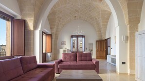 A spacious living room with a high arched ceiling, two sofas, a wooden coffee table, and a chandelier.