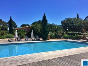 Ein rechteckiger Pool mit einer Holzterrasse, umgeben von Grünpflanzen und hohen Bäumen.