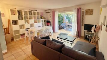 Een woonkamer met een bank, een eettafel met stoelen, een televisie en een boekenkast.