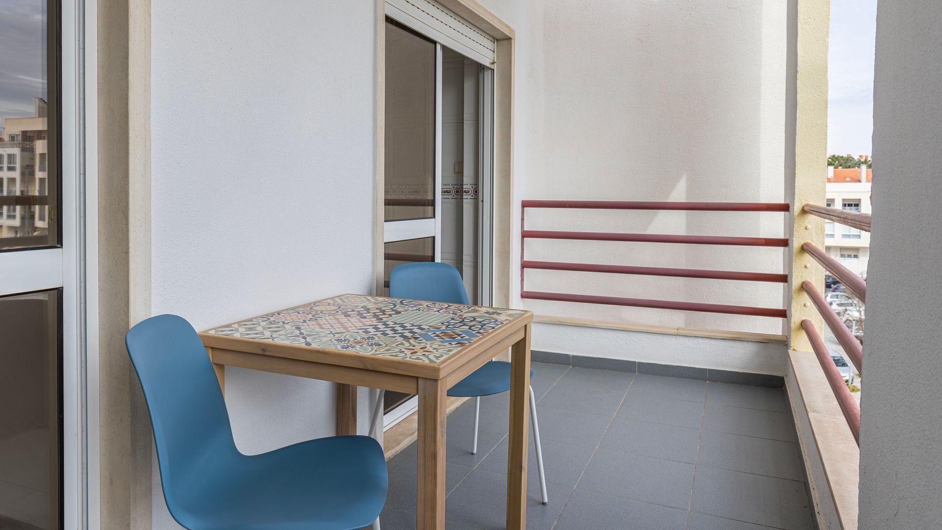 A balcony with a small table and two chairs, a sliding glass door, and a red railing.