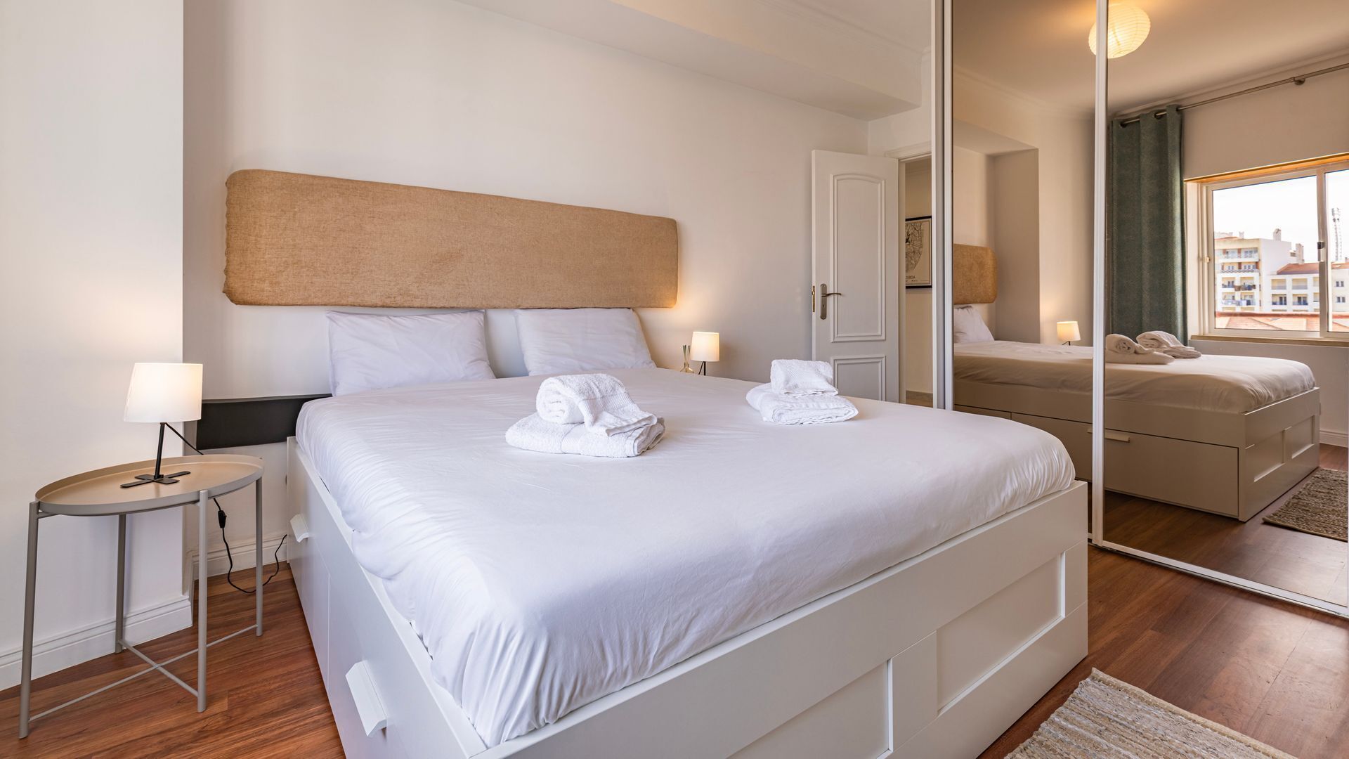 Une chambre d’hôtel avec un grand lit, des lampes de chevet, un miroir et une vue sur la ville par la fenêtre.