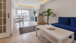 Una sala de estar moderna con un sofá azul, una mesa de centro blanca y un ventanal con vistas a edificios.