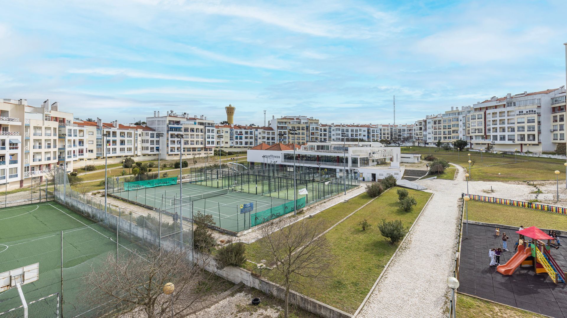 Zona residencial con edificios de apartamentos, cancha de tenis y parque infantil.