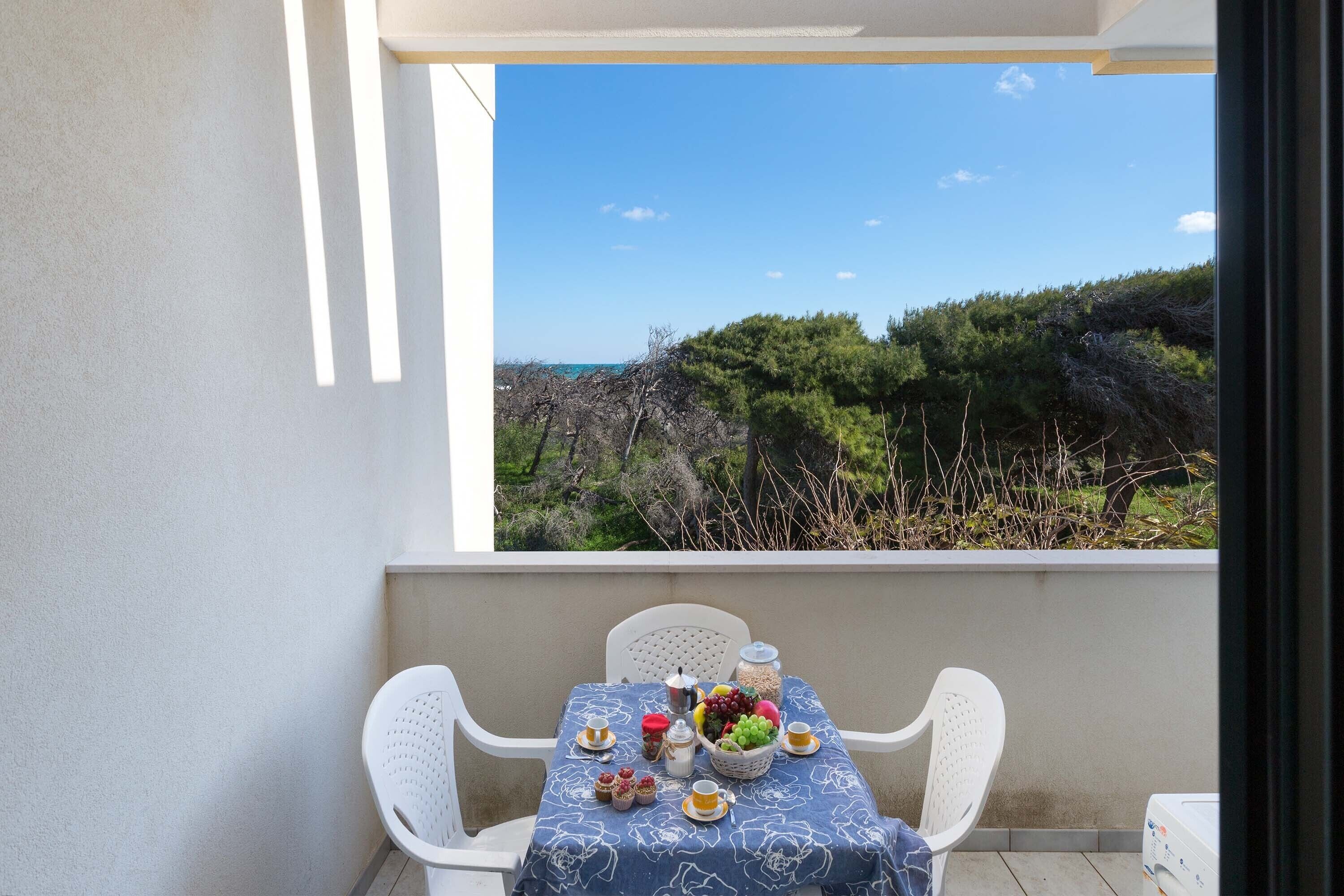 A balcony with a table set for a meal, overlooking a coastal landscape.