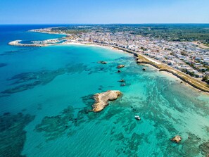 Vista aérea de un pueblo costero con un puerto deportivo, aguas turquesas cristalinas y una zona densamente poblada con edificios a lo largo de la costa.