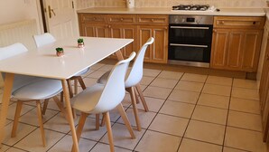 Une cuisine avec une table et des chaises blanches, des placards en bois, une cuisinière à gaz et un four.