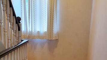A narrow hallway with a carpeted floor, a staircase with white balusters, and a window with polka dot curtains.