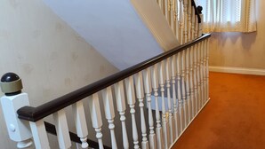 Un escalier avec des balustrades blanches et une main courante noire, menant à un palier où se trouve une porte blanche et une fenêtre avec un rideau.