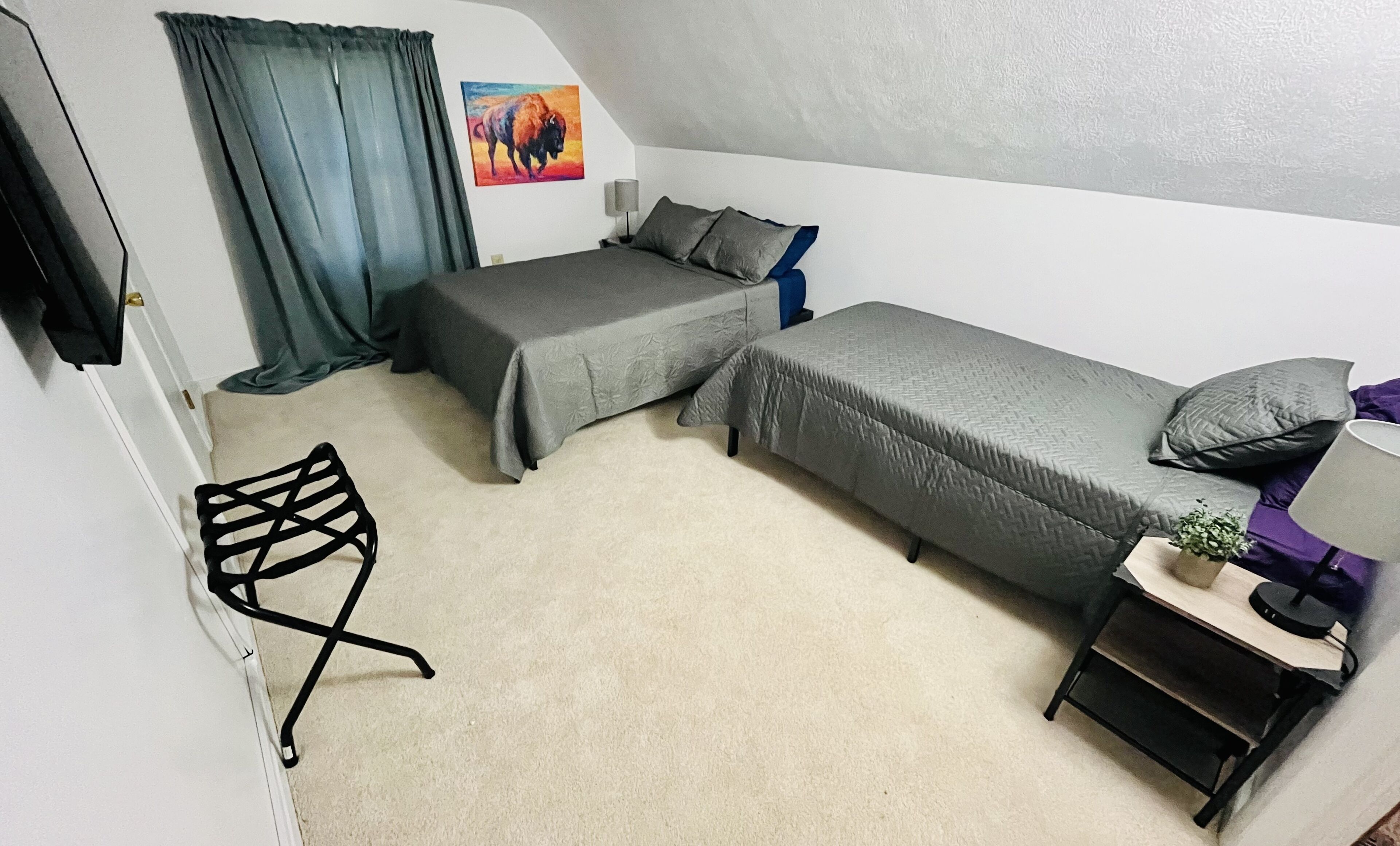 Una habitación pequeña y funcional con dos camas individuales, un escritorio, una silla y un cuadro en la pared.