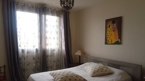 A bedroom with a bed, two pillows, a nightstand, a lamp, a painting, and a window with curtains. - House between sea and mountains located in a quiet cul-de-sac Animals accepted  (Pollestres)