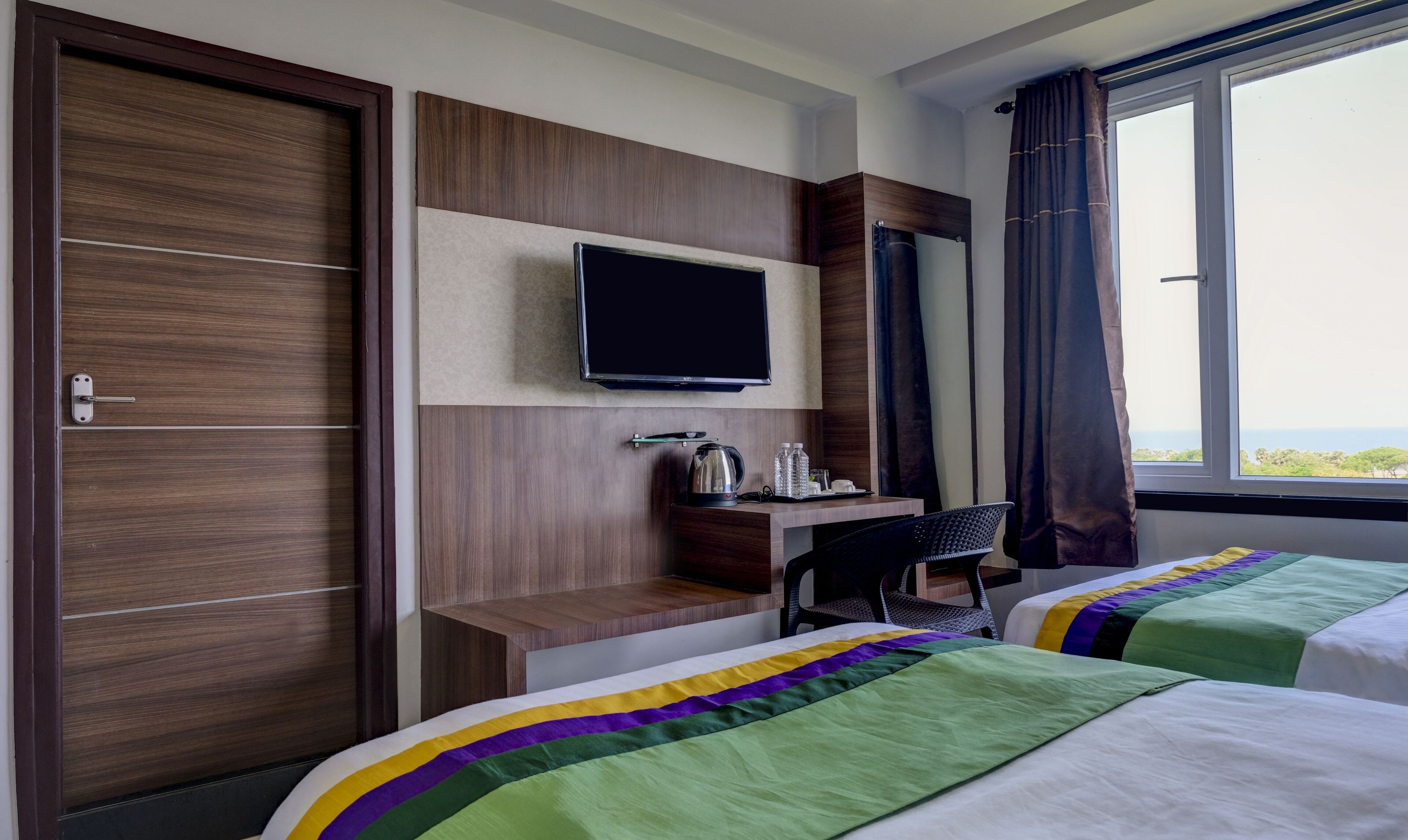 A hotel room with two beds, a desk, a television, and a view of the outdoors.