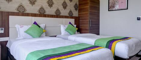 A hotel room with two beds, a wooden wardrobe, a patterned wallpaper, and a framed picture on the wall.