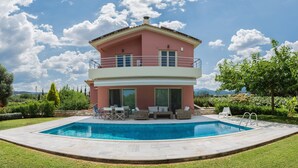 Una casa a due piani con piscina, mobili da esterno e un giardino.