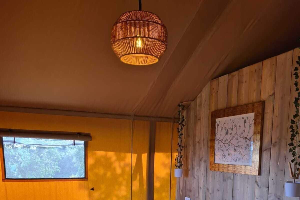 Una habitación de madera con una cama, una lámpara colgante, un ventanal y un cuadro en la pared.