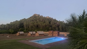 A pool area with a wooden deck, surrounded by tents and a mountain backdrop. - Glamping VALL de CODÓ (Terrades)