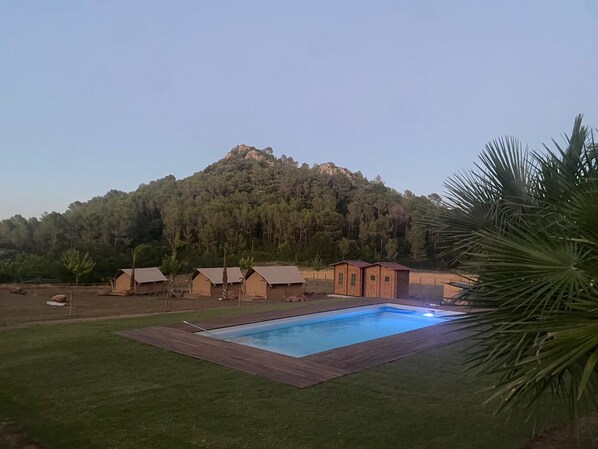 A pool area with a wooden deck, surrounded by tents and a mountain backdrop. - Glamping VALL de CODÓ (Terrades)