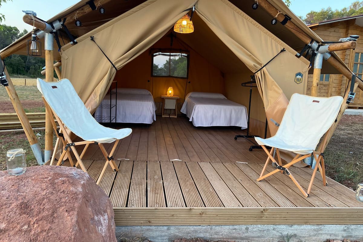 Una carpa con dos camas y dos sillas, una mesita con una lámpara y una terraza de madera.
