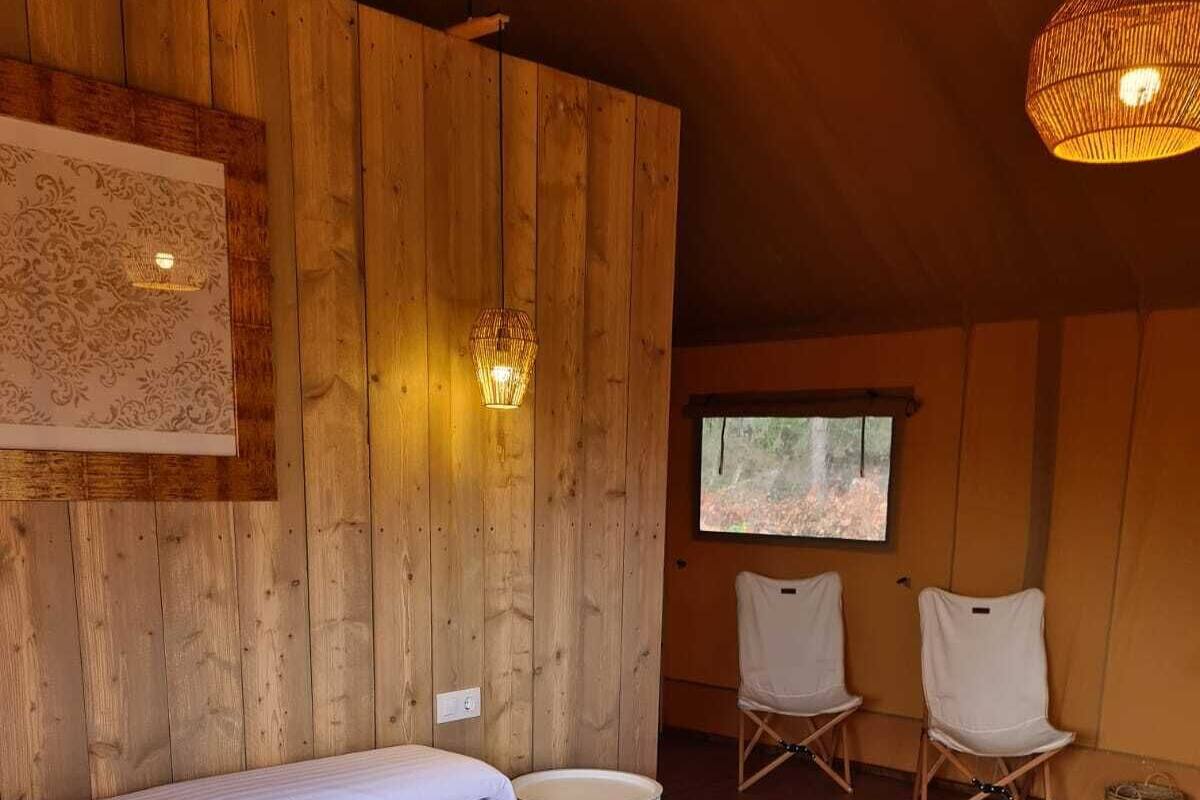 Una habitación con paneles de madera, una cama grande, dos sillas, una mesita y un ventanal.