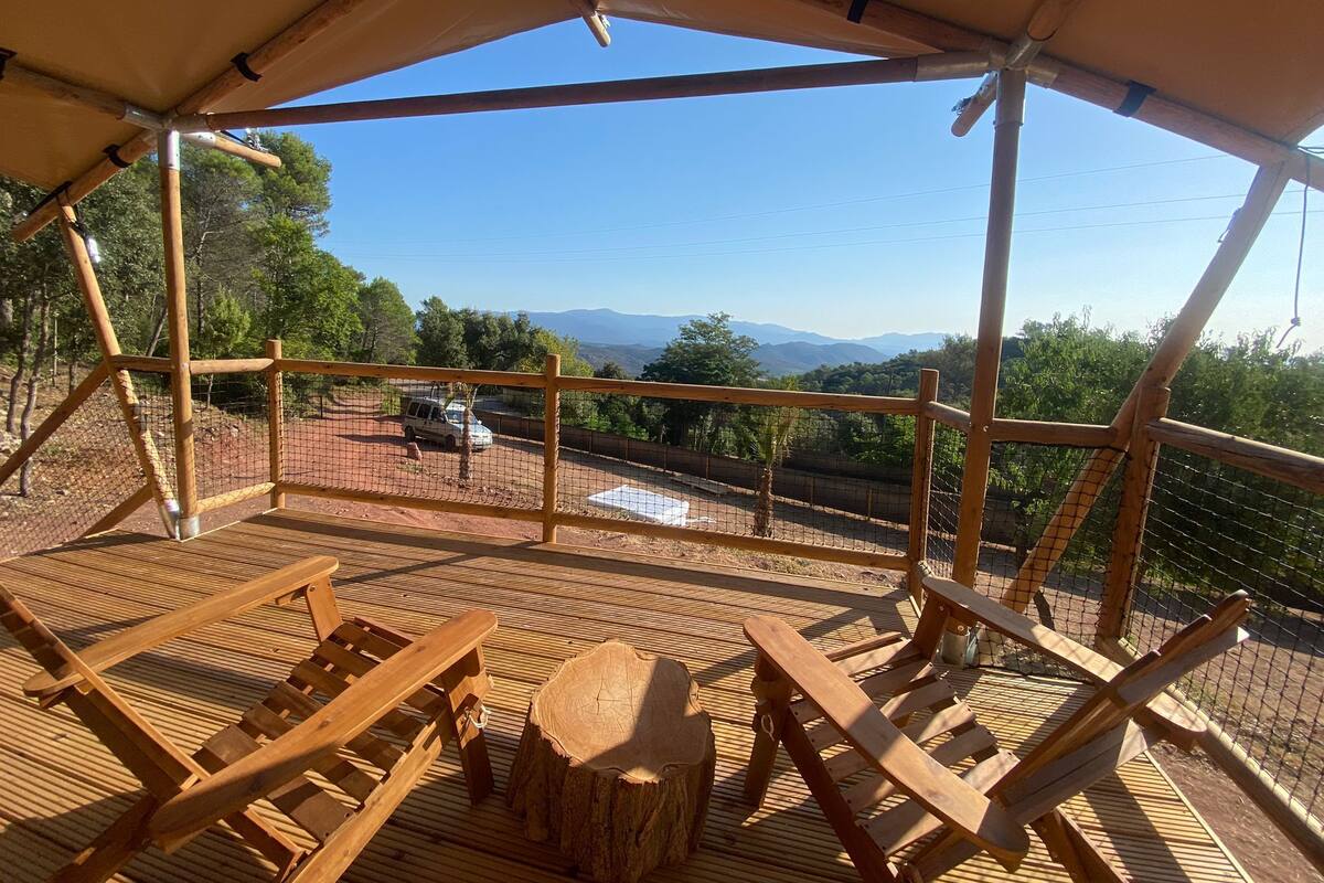 Una terraza de madera con sillones de descanso y una mesa, con vistas a un paisaje montañoso.