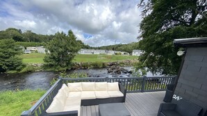 Une terrasse avec un canapé et deux fauteuils, donnant sur une rivière et la verdure environnante.