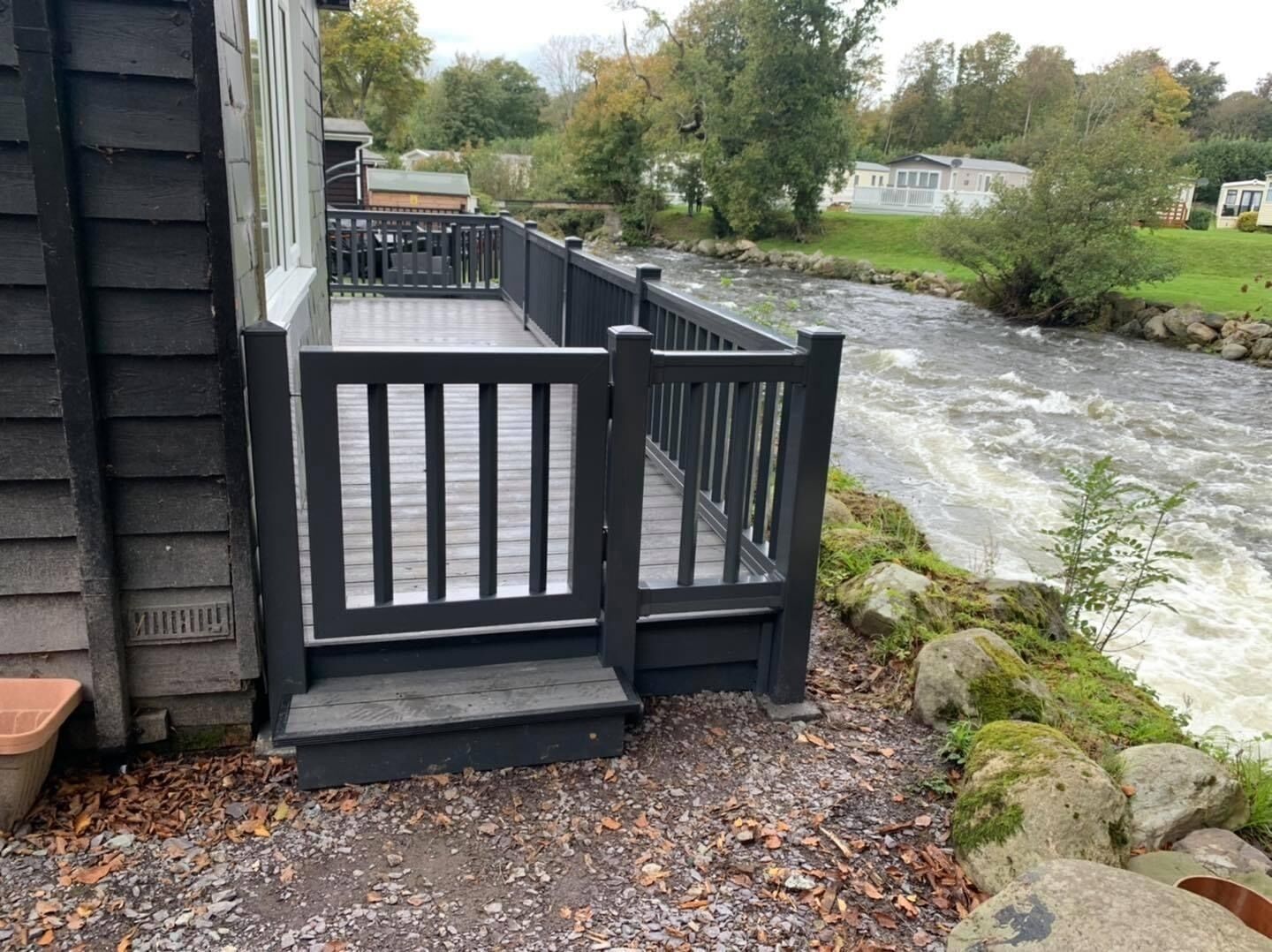 A wooden deck with a railing overlooking a river.
