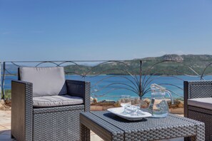 A wicker outdoor seating area with a table set for two, overlooking a scenic view of the sea and hills. - Villa Maria Dependance - Home and More (Palau)