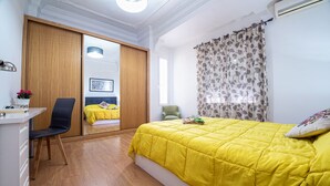 Een slaapkamer met een bed, een bureau, een stoel, een kledingkast en een raam met gordijnen.