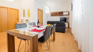 Een moderne eethoek met een glazen tafel, houten stoelen en een zwarte bank op de achtergrond.