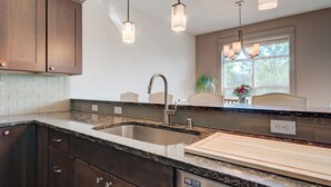 A modern kitchen with dark wood cabinets, granite countertops, a double sink, and pendant lighting.