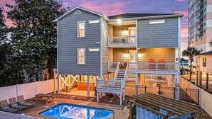 A two-story building with a pool, outdoor seating, and a balcony. - Luxe Home w/ Free Htd Pool, 50 Steps to Beach, Elevator, Putting Green, Tiki Bar (North Myrtle Beach)