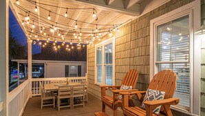 A wooden deck with a table and chairs, string lights, and a view of the city at dusk. - Luxe Home w/ Free Htd Pool, 50 Steps to Beach, Elevator, Putting Green, Tiki Bar (North Myrtle Beach)