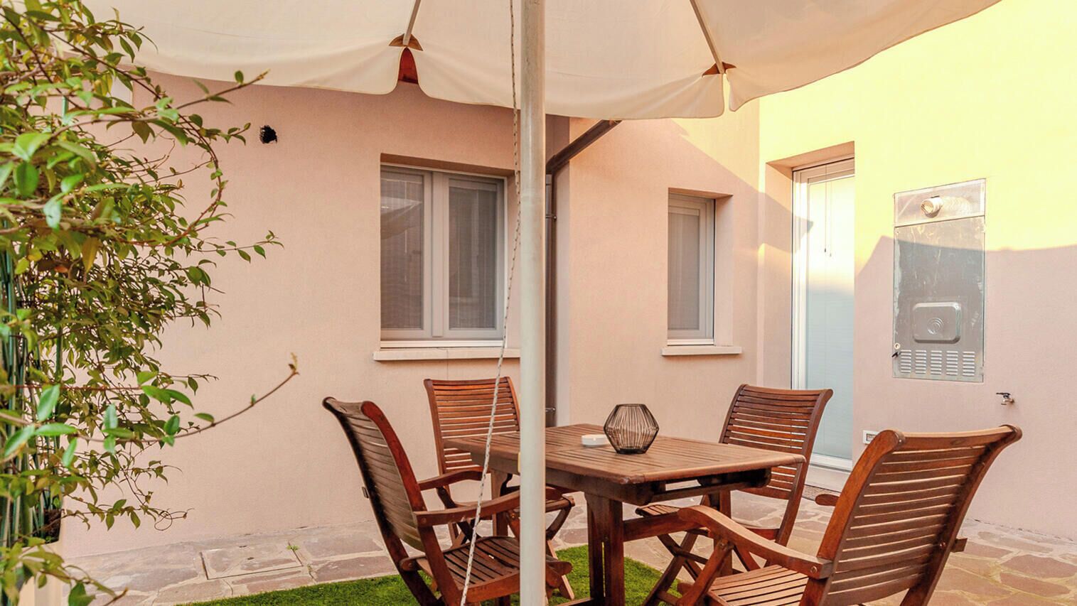 A patio with a table and chairs, a hanging umbrella, and a small garden area.