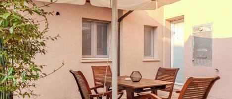 A patio with a table and chairs, a hanging umbrella, and a small garden area.