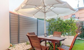 Eine Terrasse im Freien mit Tisch und Stühlen, einem großen Sonnenschirm und einem Gartenbereich.