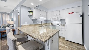 A modern kitchen with white cabinets, a granite countertop, and a stainless steel refrigerator. - Sea Cabins 9B - Heated Community Pool, Private Beach Access, Bikes Included! (Miramar Beach)