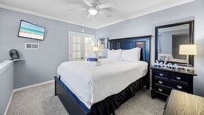 A hotel room with a bed, a ceiling fan, a TV, a bedside table with a lamp, and a dresser. - Sea Cabins 9B - Heated Community Pool, Private Beach Access, Bikes Included! (Miramar Beach)