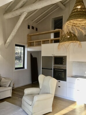 Uma cozinha moderna com forno embutido e geladeira, uma cadeira branca e uma janela com vista para árvores.