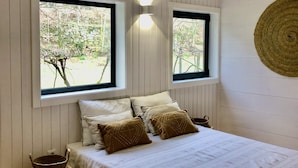 A bedroom with a bed, two windows, a woven basket, and a woven wall hanging. - Geres National Park barn (Arcos Valdevez)