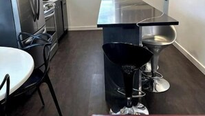 A modern kitchen with stainless steel appliances, a dining area with a white table and black chairs, and a red cushioned bench. - Modern Ranch near Knapp Center, Stadium, Downtown (Des Moines)