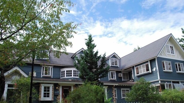 A two-story house with a gabled roof, a front porch, and a white picket fence.