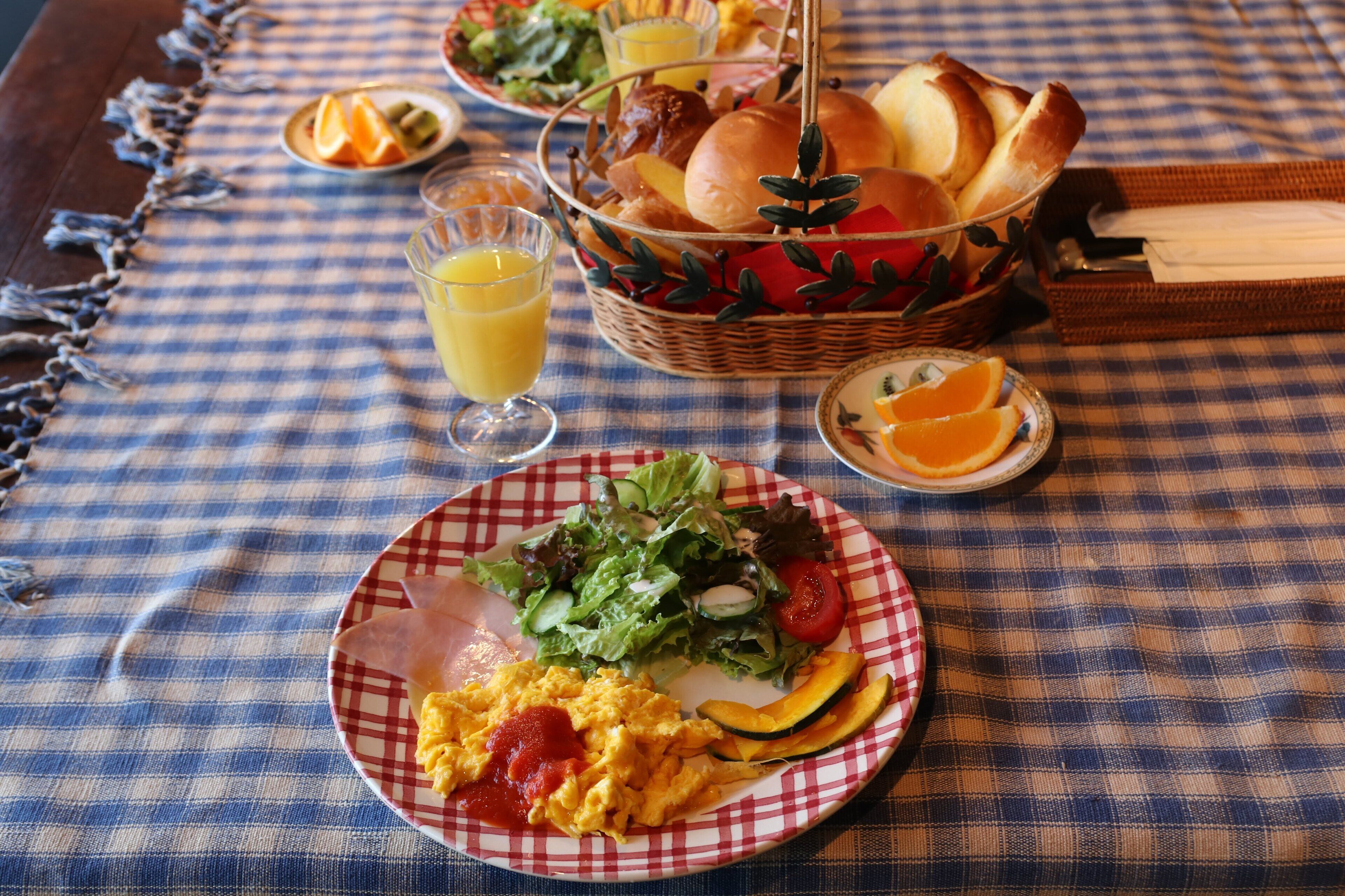 A checkered tablecloth with a plate of scrambled eggs, a salad, and a basket of bread.