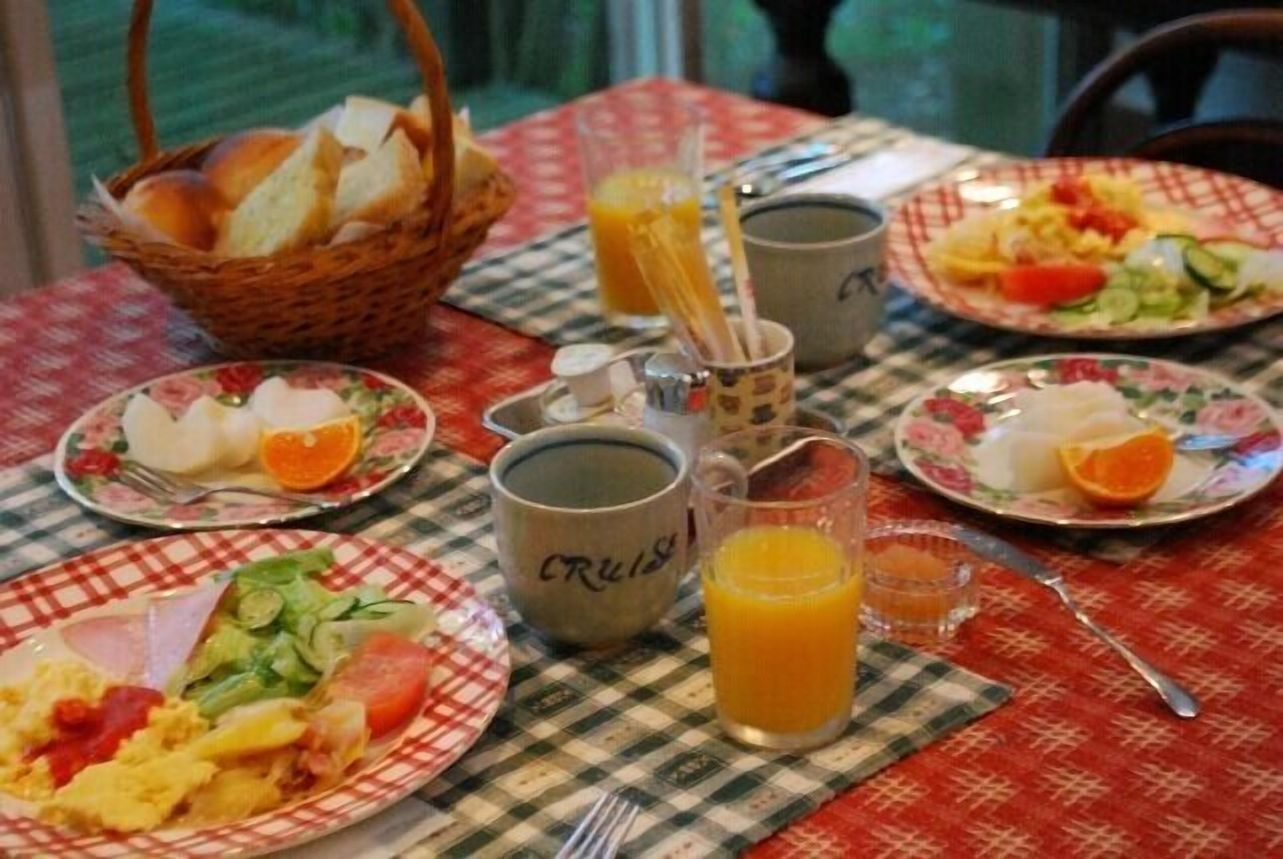 Una mesa de desayuno con platos de comida, una cesta de pan y dos tazas con la etiqueta 'CRUS'.