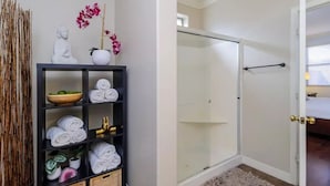 Un baño con cabina de ducha de vidrio, una puerta blanca y una cama visible a través de la puerta.