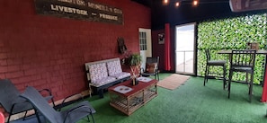 A room with a red brick wall, a patterned sofa, a wooden coffee table, and a green artificial turf floor. - Renovated historical barn in Malpeque.. close to several beaches and Cabot Park. (Malpeque)