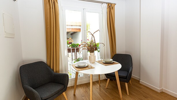 A dining area with two chairs, a round table, and a view of a balcony with plants and a wooden structure. - 7escalones Apartamentos Boutique (Rota)