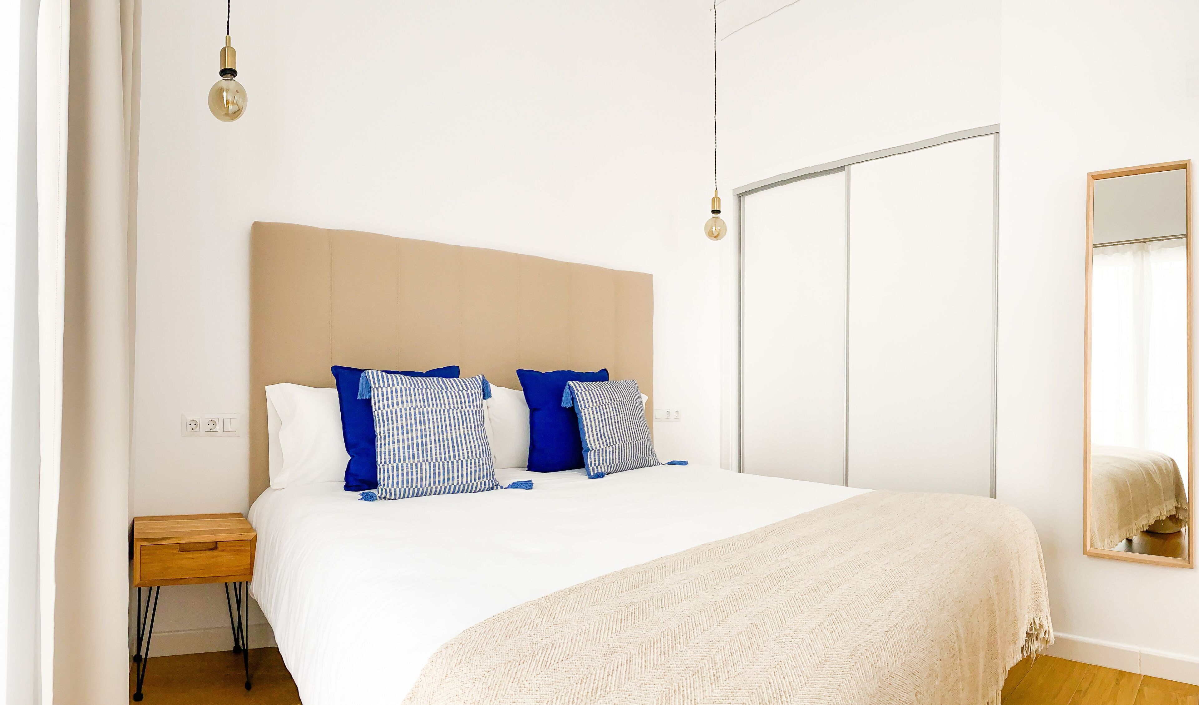 A bedroom with a bed, bedside table, and a mirror on the wall.