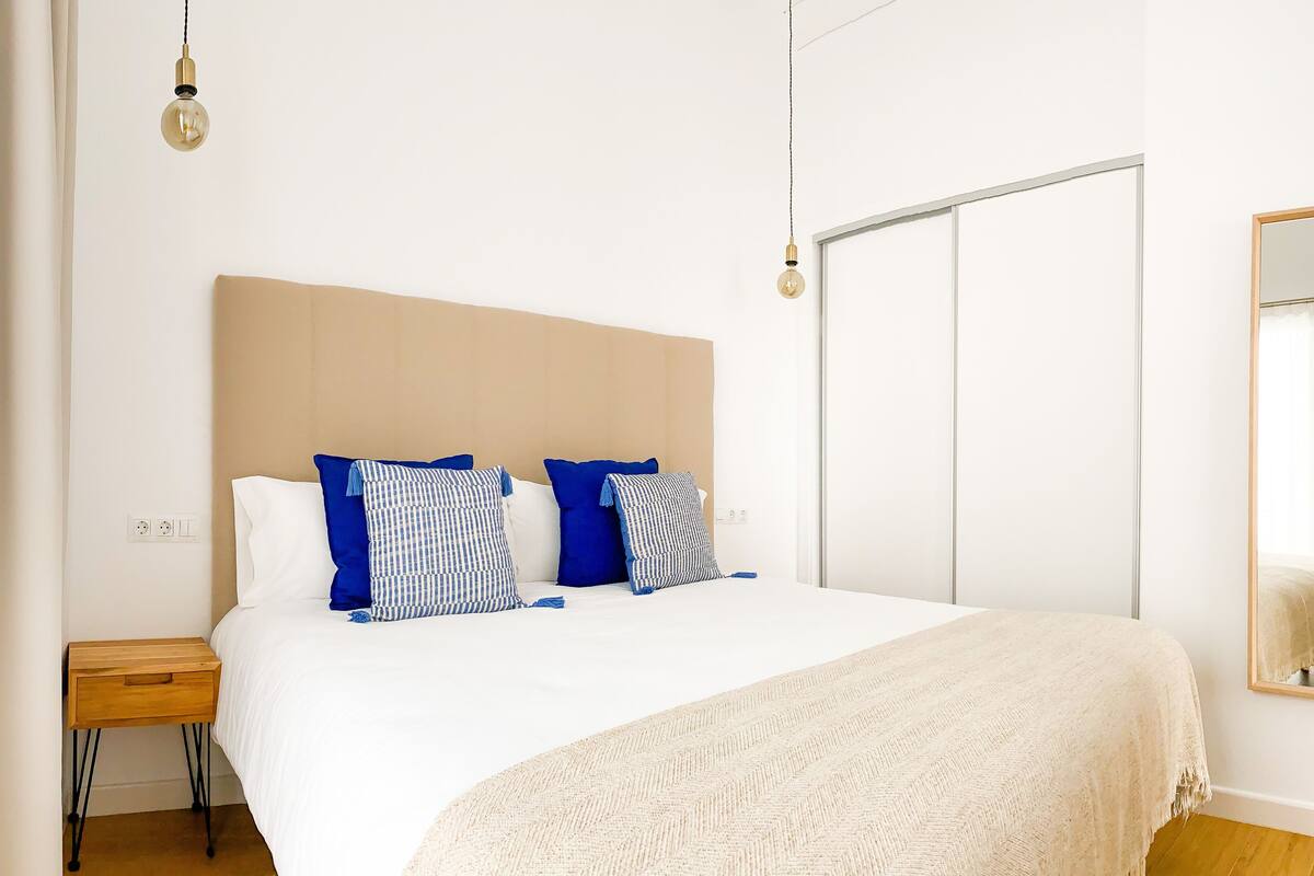 A bedroom with a bed, bedside table, and a mirror on the wall.